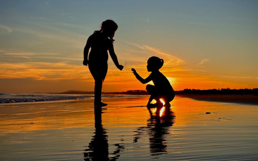 A parent and child playing at the water&rsquo;s edge at sunset
